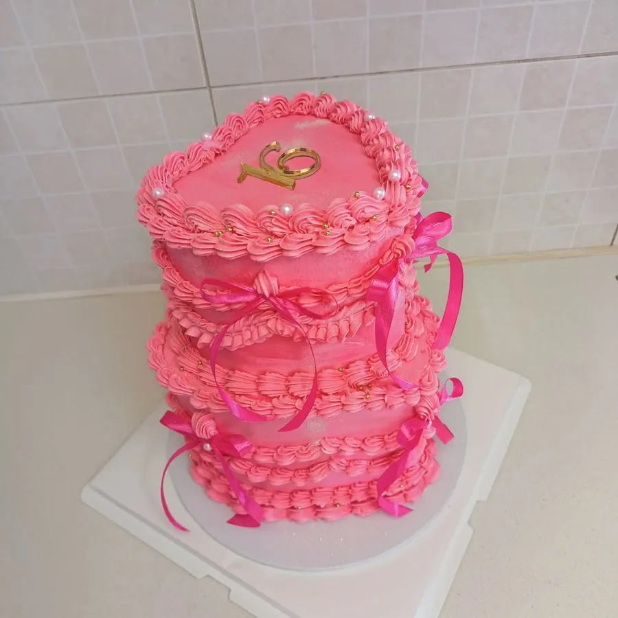Pink vintage-style heart cake with ruffled piping, gold pearls, and satin bows