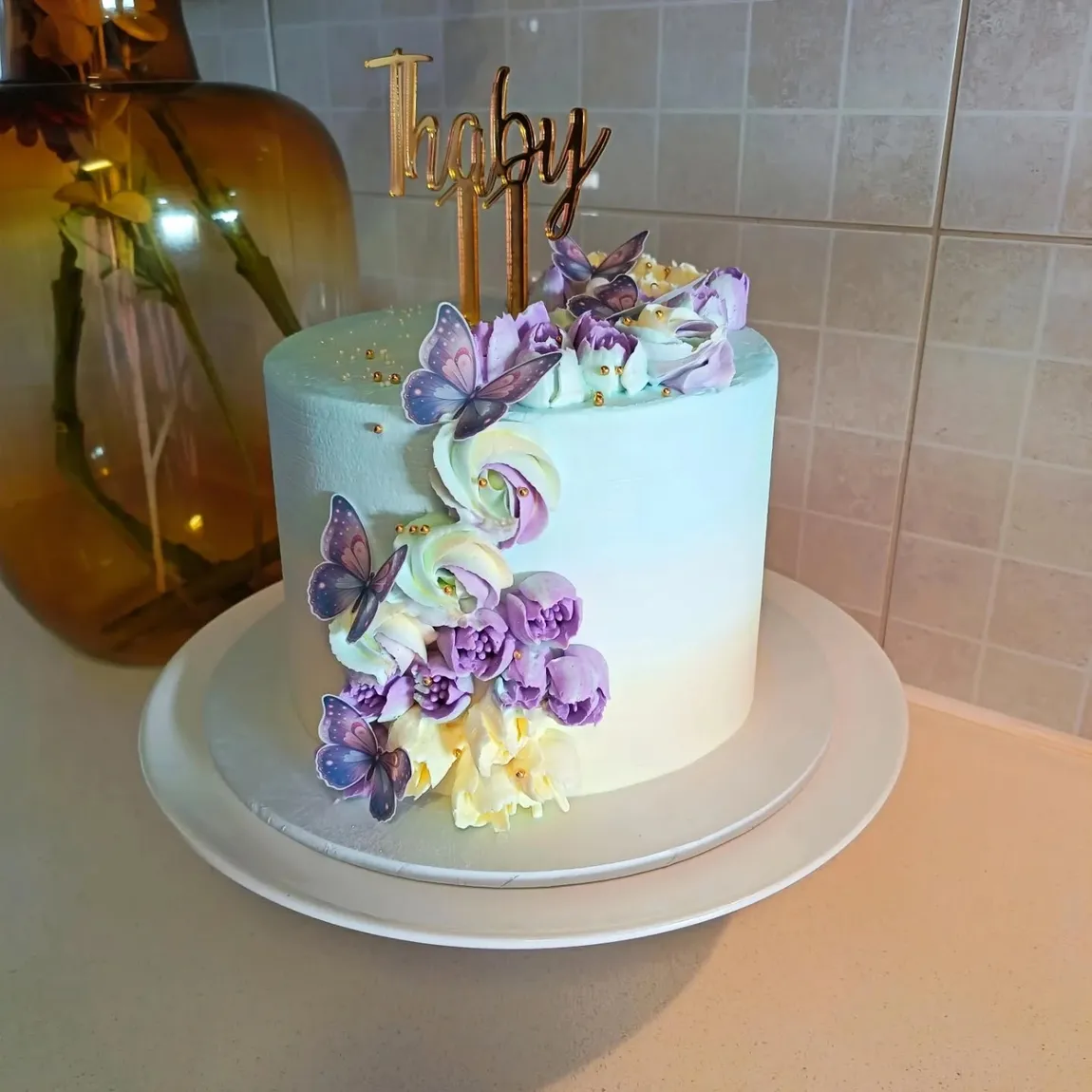 Mint buttercream cake with lilac piped flowers, butterflies, and a gold name topper